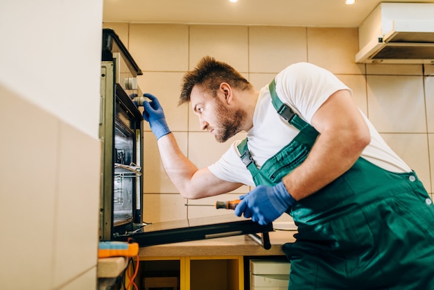 Il tecnico in uniforme controlla il forno, tecnico. l'operaio professionista effettua riparazioni in casa, servizio di riparazione domestica