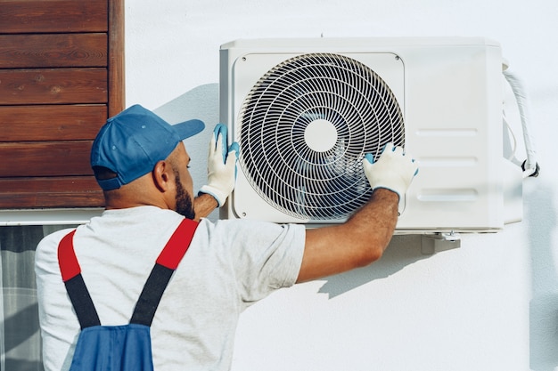 Riparatore in uniforme che installa l'unità esterna del condizionatore d'aria