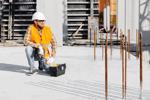 Repairman worker in uniform and helmet working with cordless screwdriver and tool box