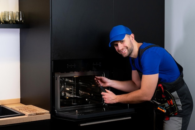 Repairman a worker in uniform inspects the oven with a screwdriver in the kitchen the concept of rep