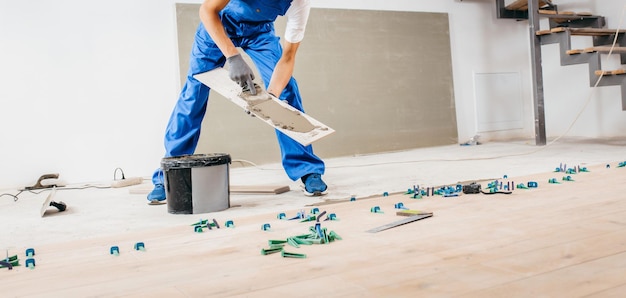 Reparateur in grijze handschoenen en speciaal uniform cement leggen op tegels in een nieuw huis