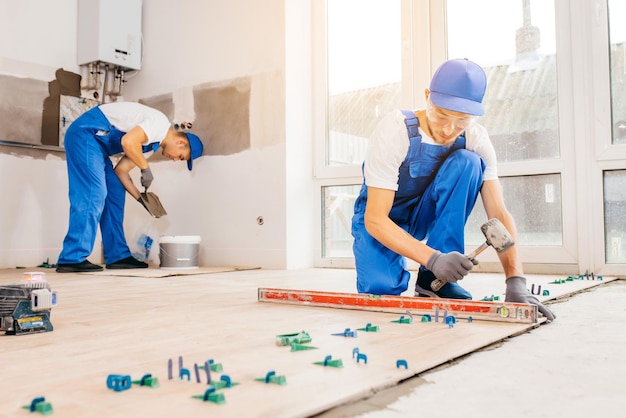 Reparateur in grijze handschoenen en uniforme tegels met tegelnivelleersysteem op de vloer in huis