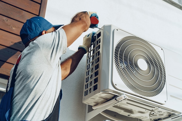 Reparateur in uniform die de buiteneenheid van airconditioner installeert