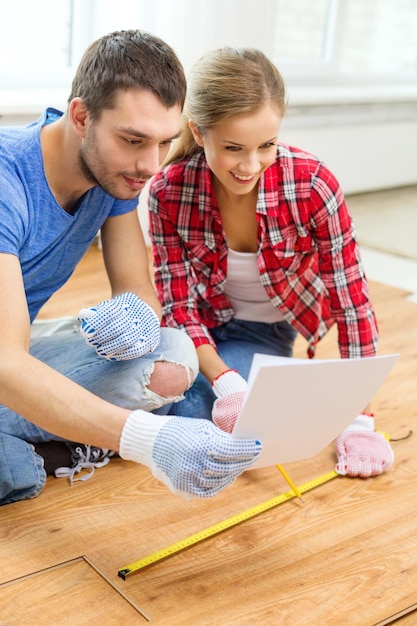 reparatie-, bouw- en huisconcept - lachend paar dat houten vloeren meet