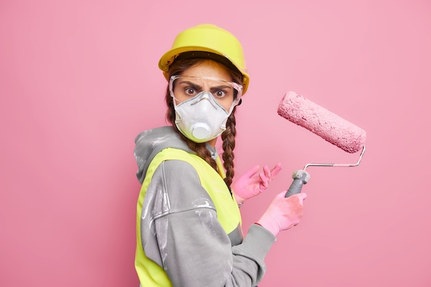 Reparatie- en onderhoudsservice. Ernstige drukke vrouwelijke bouwer repareert huis verft muren met roller