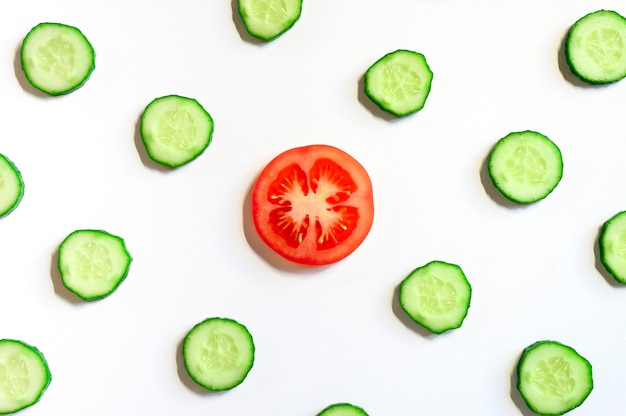 Repeating pattern of sliced semicircles of fresh raw vegetable cucumbers for salad and a slice of tomato in the center isolated on a white background flat lay, top view