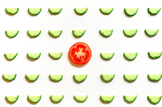 Repeating pattern of sliced semicircles of fresh raw vegetable cucumbers for salad and a slice of tomato in the center isolated on a white background flat lay, top view