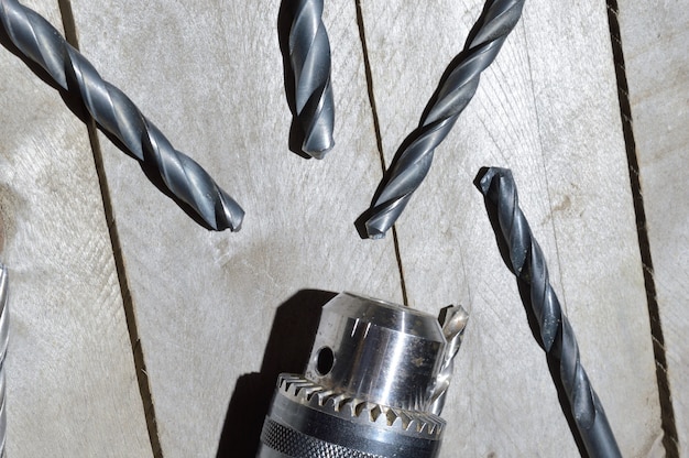 Replaceable drill chuck and old drill bits lie on a wooden plank background. close-up.