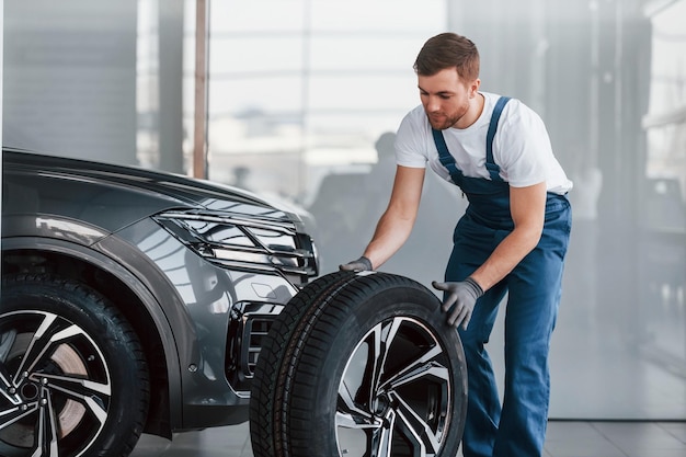 Replacement of wheel Young man in white shirt and blue uniform repairs automobile