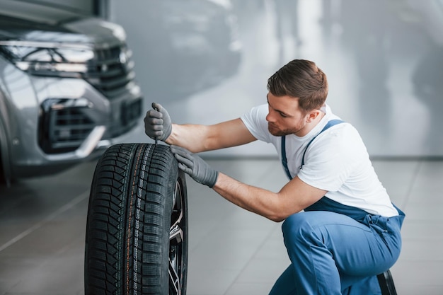 Replacement of wheel Young man in white shirt and blue uniform repairs automobile