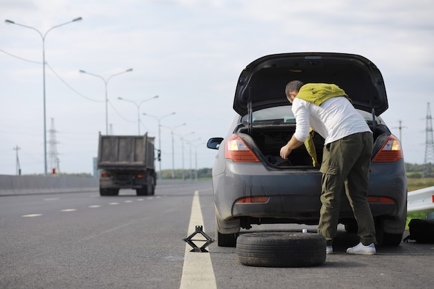 道路上の車のホイールを交換します。傍観者としてタイヤの仕事をしている男性。