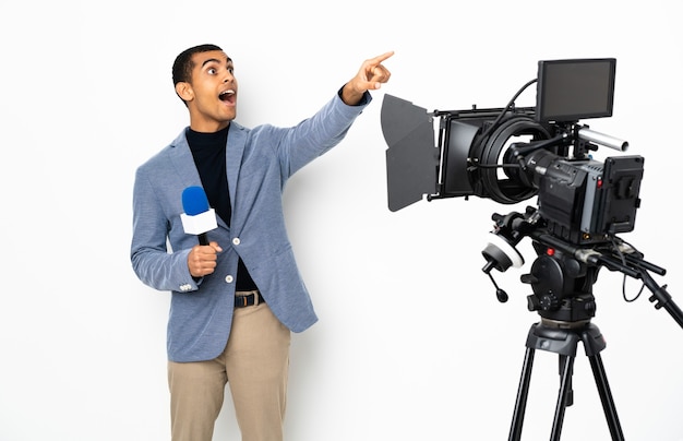 Reporter African American man holding a microphone and reporting news over isolated white background pointing away