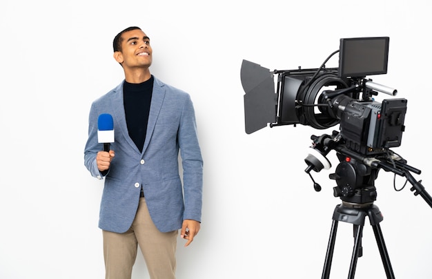 Reporter African American man holding a microphone and reporting news over isolated white wall thinking an idea while looking up