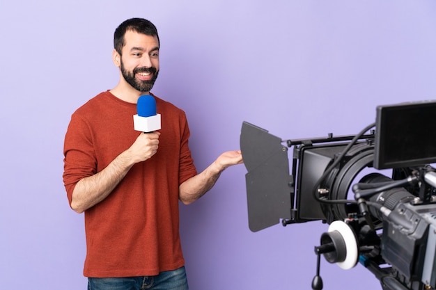 Репортер мужчина держит микрофон и сообщает новости над изолированной фиолетовой стеной