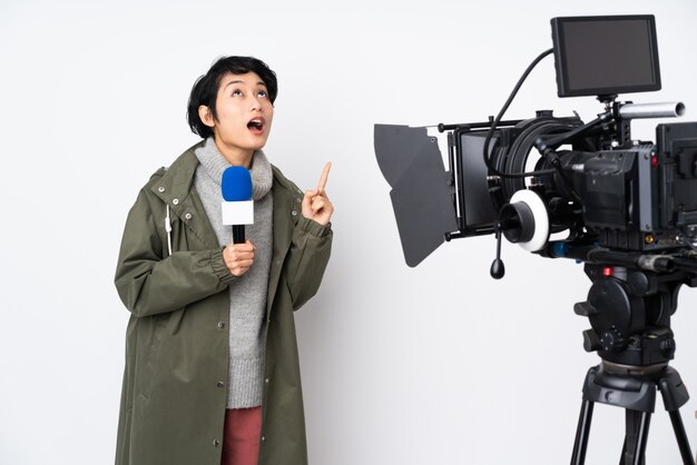 Reporter vietnamese woman holding a microphone and reporting news pointing up and surprised