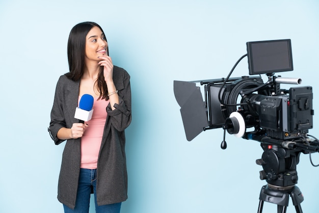 Reporter woman holding a microphone and reporting news on blue looking to the side