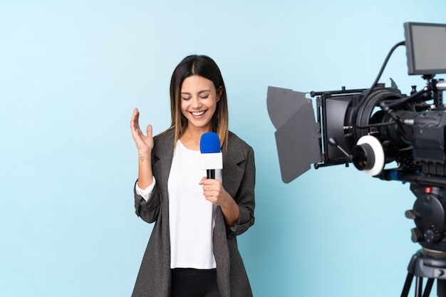 Reporter woman holding a microphone and reporting news over blue wall laughing