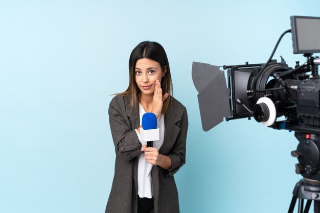 Reporter woman holding a microphone and reporting news over isolated blue wall whispering something