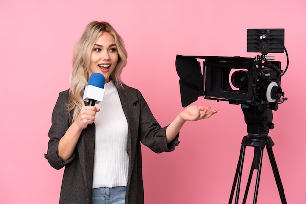 Reporter woman holding a microphone and reporting news over isolated pink wall