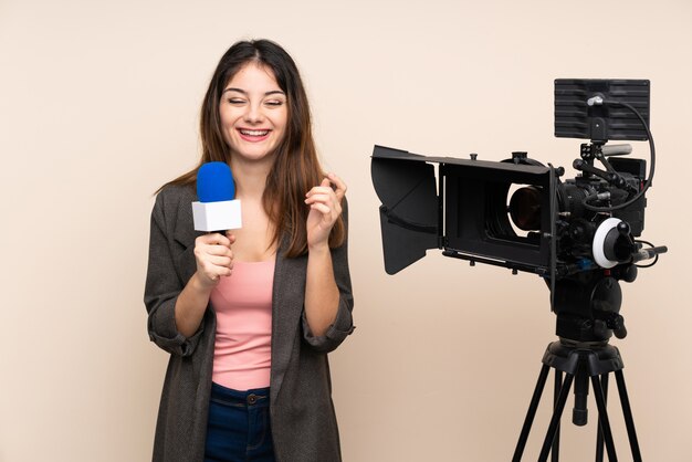 Reporter woman holding a microphone and reporting news over isolated wall laughing