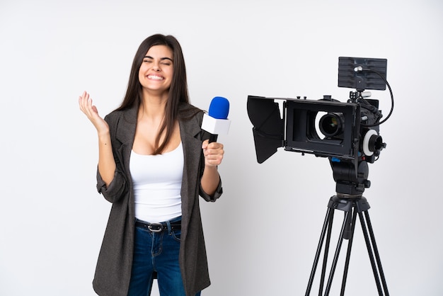 Reporter woman holding a microphone and reporting news over isolated white wall laughing