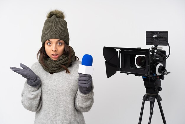 Reporter woman holding a microphone and reporting news over isolated white wall making doubts gesture