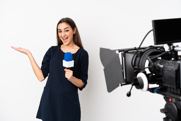 Reporter woman holding a microphone and reporting news isolated on white wall with shocked facial expression