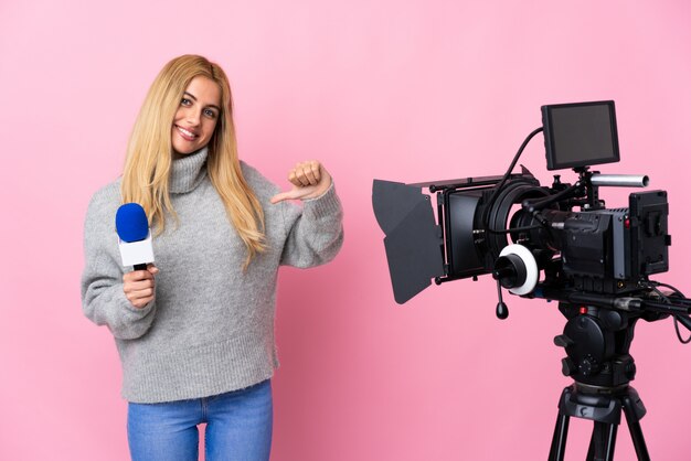 Reporter woman holding a microphone and reporting news over pink wall proud and self-satisfied