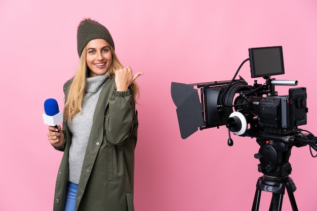 Reporter woman holding a microphone and reporting news over pink wall with thumbs up gesture and smiling