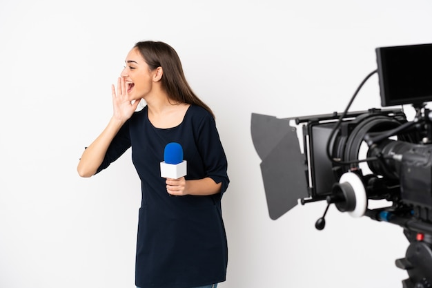 Reporter woman holding a microphone and reporting news on white wall shouting with mouth wide open to the lateral