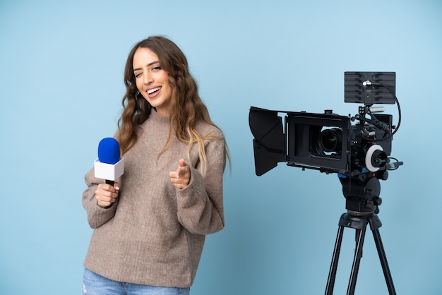 Reporter young woman holding a microphone and reporting news points finger at you