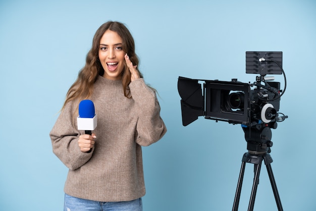 Reporter young woman holding a microphone and reporting news shouting with mouth wide open