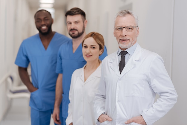 Foto rappresentare il mio staff internazionale. piacevole medico esperto con la barba che si gode il lavoro in clinica e presenta i membri del personale mentre sorride