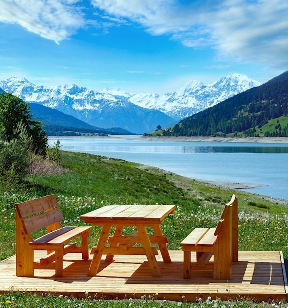 Reschensee ( or Lake Reschen) summer landscape with blossoming meadow and picnic wooden bench (Italy).