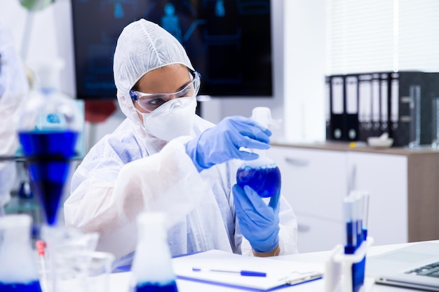 Researcher analyzes a tube with a blue liquid from which smoke comes out. Surrounded by other tubes