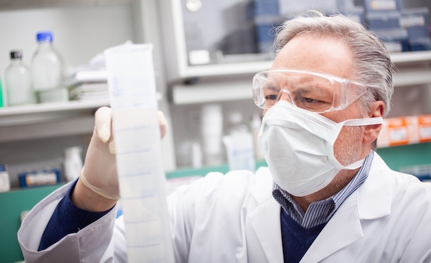Исследователь держит колбу с синей жидкостью в лаборатории, концепция исследования коронавируса