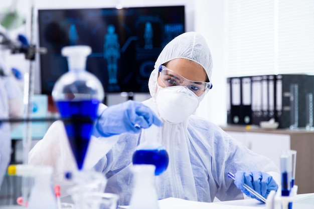 Researcher mixing a blue liquid in a tube and holding a pen in his hand