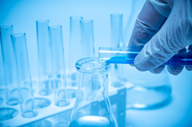 A researcher's hand holding a test tube containing blue liquid.