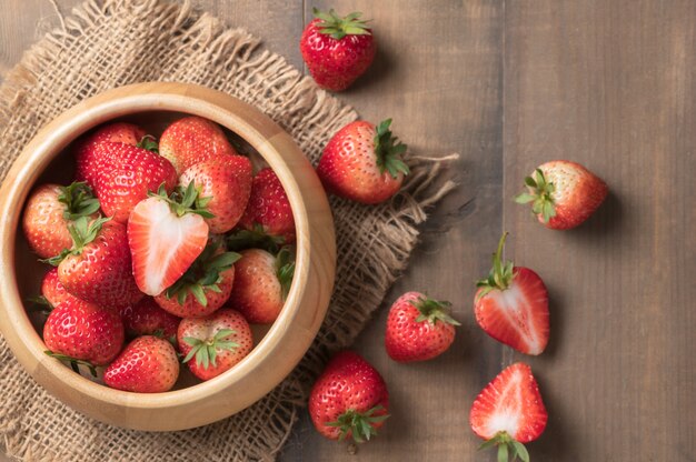 resh sliced Red berry strawberries in wood bowl on old wood background, diet fruits concept