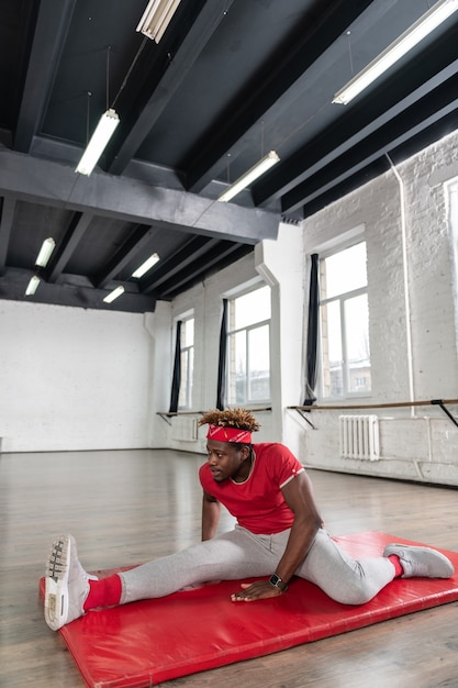 Foto risoluto uomo in forma dai capelli corti che allunga le gambe per lo spago mentre è solo nella sala sportiva