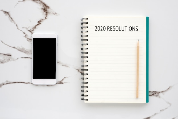 Resolutie 20120 op blanco notebookpapier slimme telefoon met leeg scherm op witte marmeren achtergrond