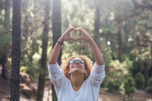 Foto rispetta la natura all'aperto e salva il concetto di mondo delle foreste con una bella donna adulta che guarda in alto e fa il segno dell'amore del focolare con le mani