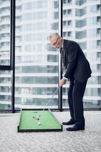 A respectable elderly man playing a mini golf in the office.