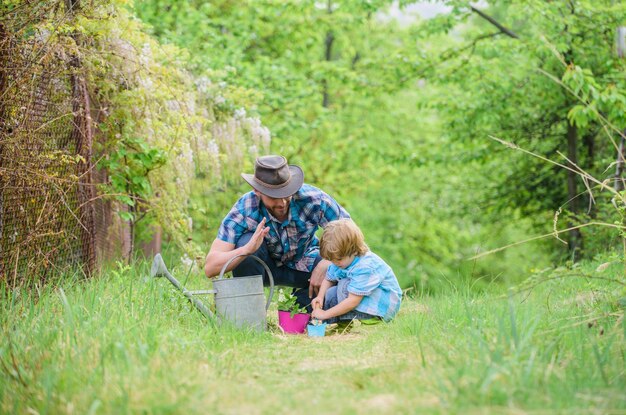 Respecting ecology small boy child help father in farming Eco farm father and son in cowboy hat on ranch watering can pot and hoe Garden equipment happy earth day Family tree nursering