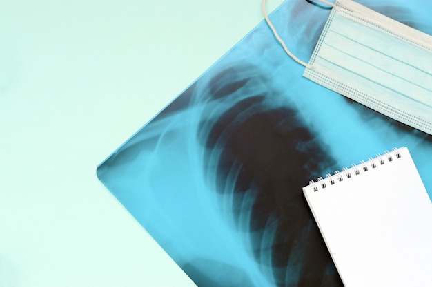 Respiratory mask and empty notepad page on x-ray of human lungs, top view