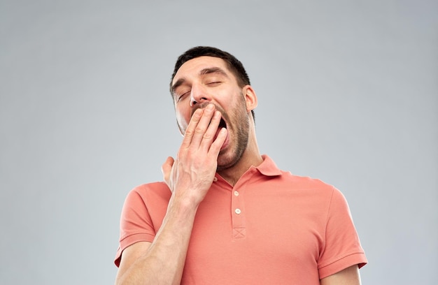 rest, bedtime and people concept - tired yawning man over gray background