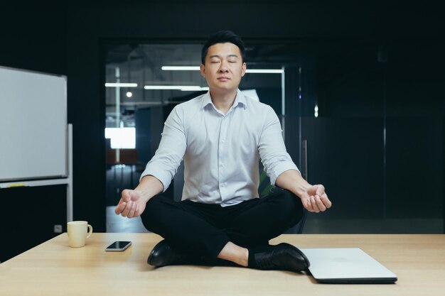 Rest break at the workplace a young asian man sits in the office on the desk in the lotus yoga