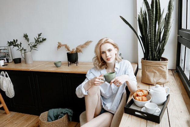 Concetto di riposo a casa. una giovane e bella donna sta facendo colazione a casa in una cucina luminosa ed elegante vicino alla finestra.