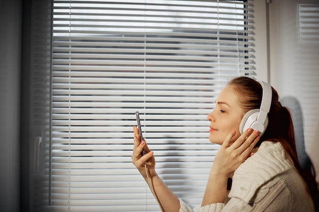 Foto riposo e rilassamento, giovane donna caucasica che ascolta la musica in cuffie facendo uso di uno smartphone