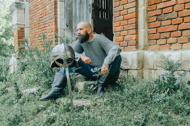 Rest of Viking warrior near an old brick castle and trees Sword and helmet Pensive look Old door